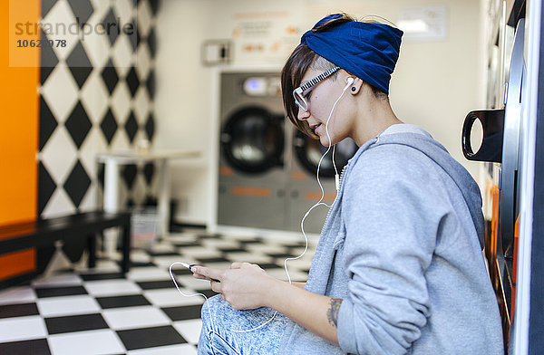 Junge Frau hört Musik mit Kopfhörern im Waschsalon