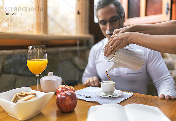 Mann beim Frühstück  während Frau Kaffee in seine Tasse gießt