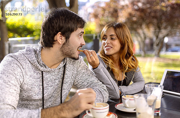 Junge Frau  die ihren Freund in einem Straßencafé füttert.