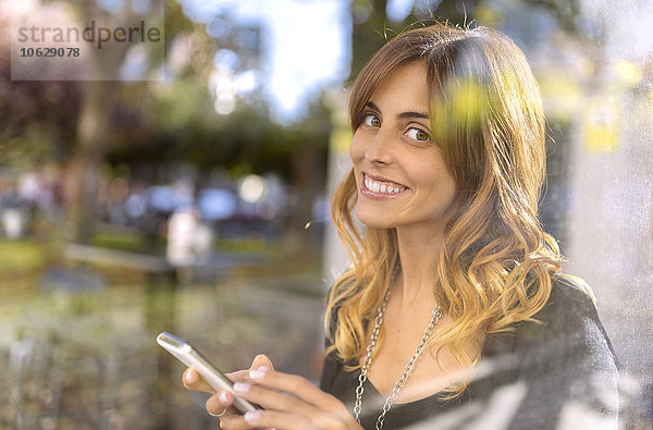 Porträt einer lächelnden jungen Frau mit Smartphone