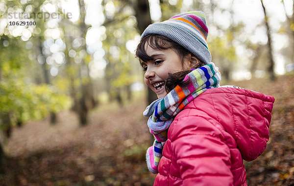 Glückliches kleines Mädchen im Wald mit Mütze und Schal im Herbst