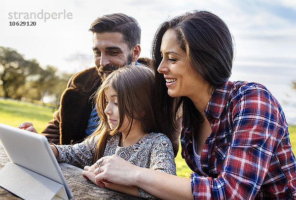 Glückliche Eltern mit der Tochter  die im Freien ein digitales Tablett benutzt.