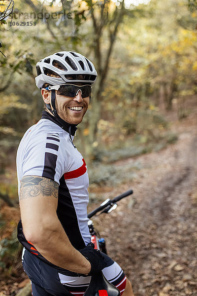 Portrait des lächelnden Mountainbikers mit Fahrradhelm und Sonnenbrille im Wald