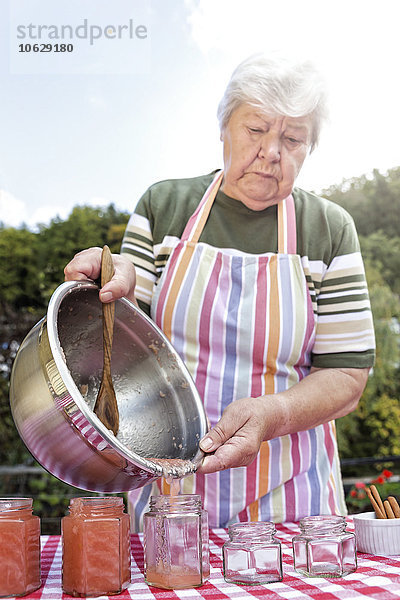 Seniorin gießt hausgemachtes Apfelmus in Marmeladengläser