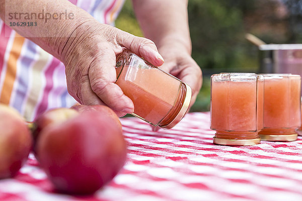 Seniorenfrau dreht Glas hausgemachte Apfelmus  Nahaufnahme