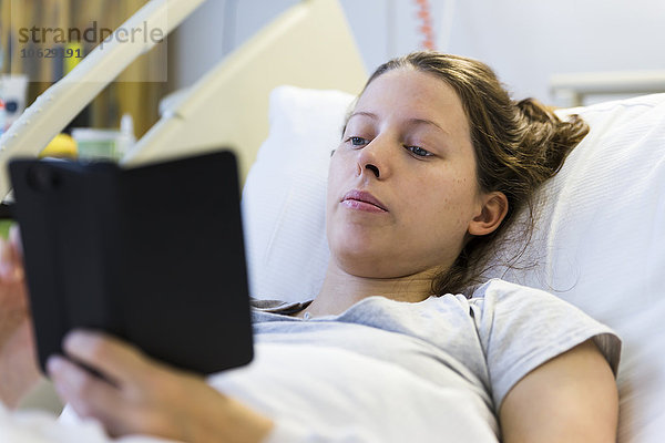 Frau liegt im Krankenhausbett und schaut auf das Smartphone