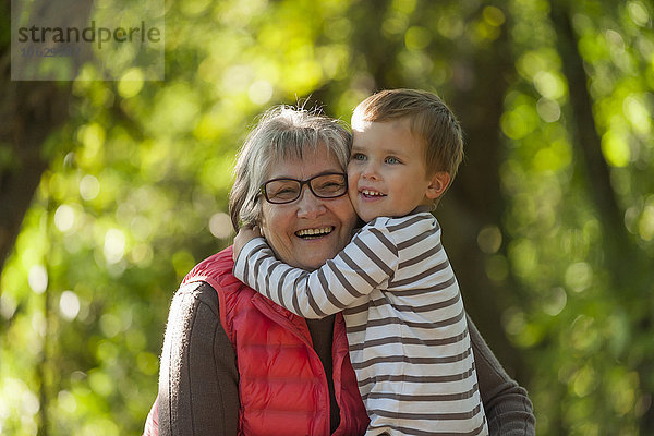 Lächelnder kleiner Junge  der seine glückliche Großmutter umarmt.