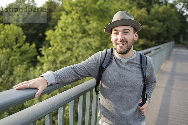 Porträt eines bärtigen jungen Mannes mit Hut auf einer Brücke stehend