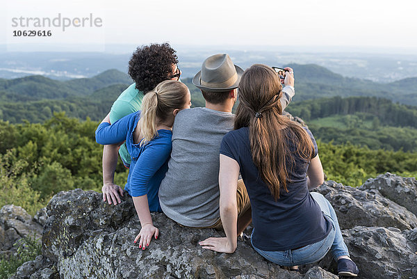 Deutschland  Siebengebirge  Rückansicht von vier Freunden  die einen Selfie mit Smartphone auf dem Mount Olivet nehmen.