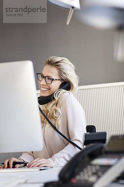 Lächelnde blonde Frau im Büro am Telefon