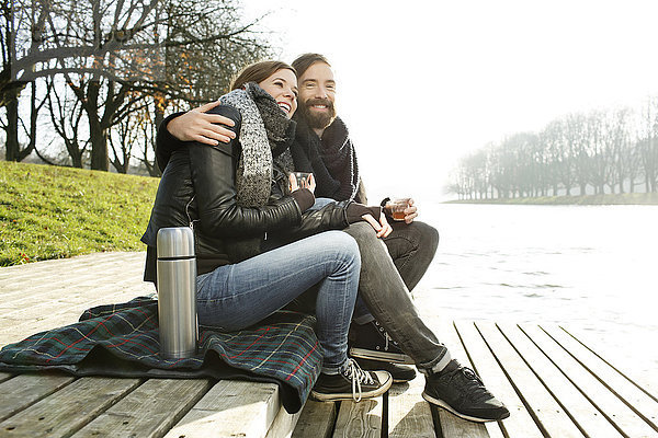 Glückliches Paar mit heißem Getränk am Flussufer im Herbst