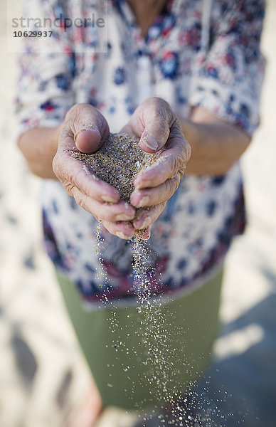 Hände einer älteren Frau  die Sand am Strand hält.