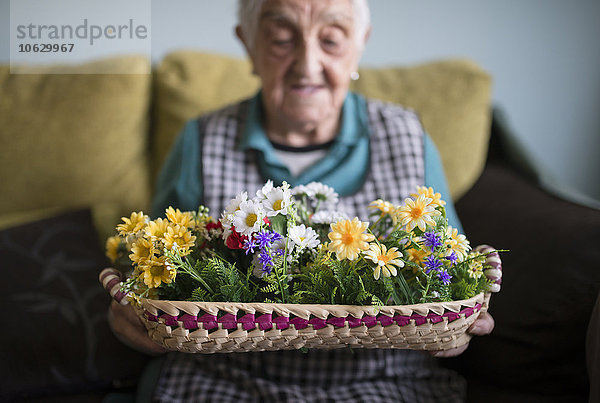 Seniorenfrau zeigt einen mit Kunstblumen geschmückten Korb