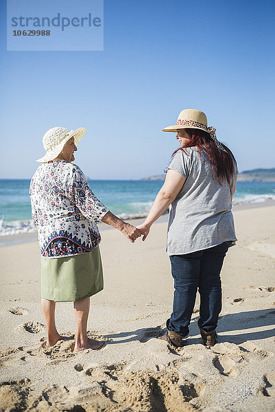 Großmutter und erwachsene Enkelin halten sich an einem sonnigen Tag an den Strand.
