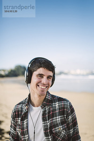 Spanien  La Coruna  Porträt eines lächelnden Mannes mit Kopfhörern am Strand