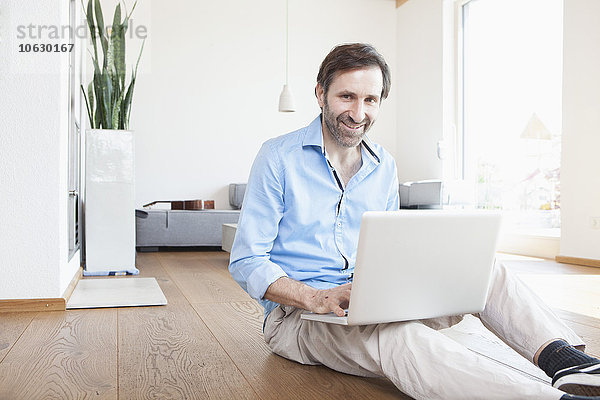 Erwachsener Mann zu Hause mit Laptop auf dem Boden sitzend