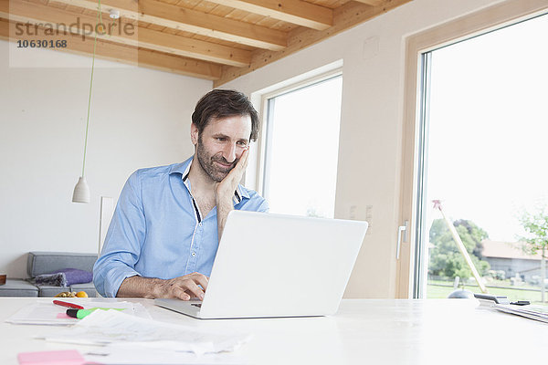 Erwachsener Mann  der von zu Hause aus mit dem Laptop arbeitet.