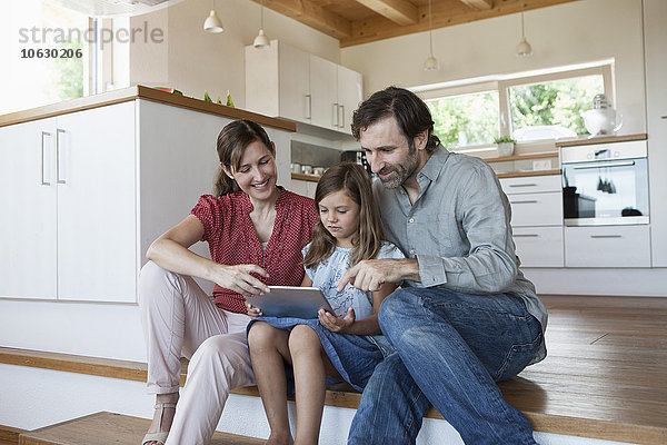 Fröhliche Familie auf Küchenstufen sitzend  Tochter mit digitalem Tablett