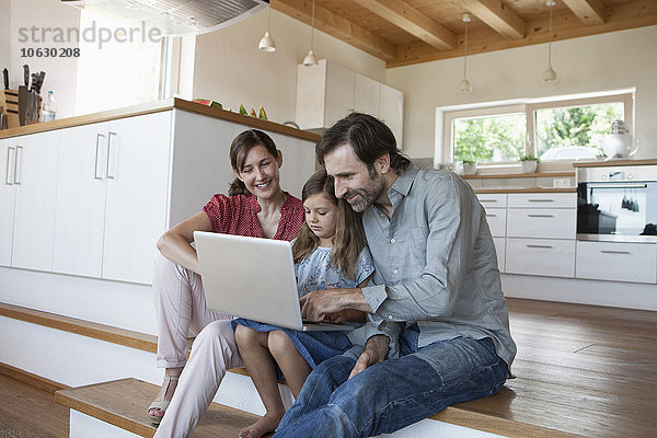 Glückliche Familie sitzend auf Küchenstufen  Tochter mit Laptop