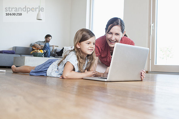 Mutter und Tochter liegen auf dem Boden mit Laptop  Vater macht Musik im Hintergrund