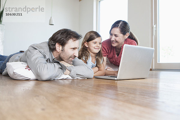 Glückliche Familie auf dem Boden liegend  mit Laptop