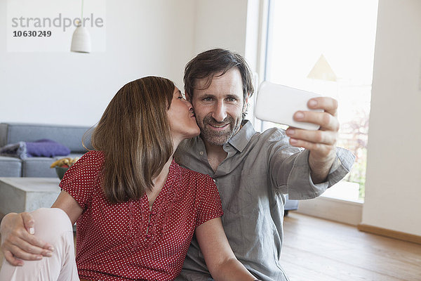 Erwachsenes Paar  das auf dem Boden sitzt und Selfie mit Smartphone nimmt.