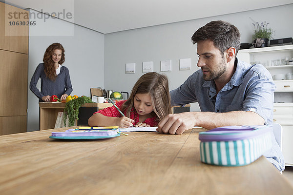 Kleines Mädchen macht Hausaufgaben am Küchentisch  während ihr Vater sie beobachtet.