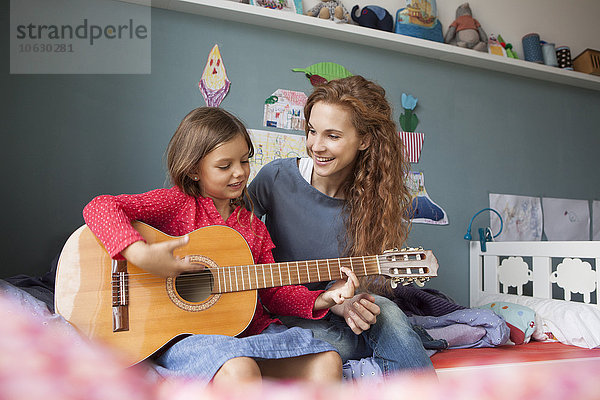 Kleines Mädchen spielt Gitarre  während ihre Mutter zuhört.