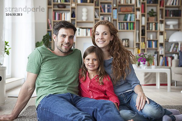 Porträt eines kleinen Mädchens und ihrer Eltern  die zusammen auf dem Boden im Wohnzimmer sitzen.