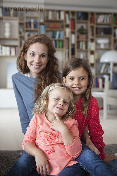 Porträt von zwei kleinen Schwestern und ihrer Mutter im Hintergrund  die im Wohnzimmer auf dem Boden sitzen.