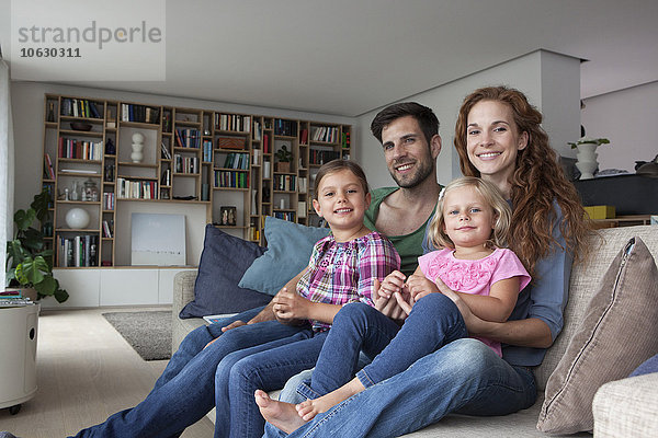 Familienporträt eines Paares mit zwei kleinen Mädchen auf der Couch im Wohnzimmer