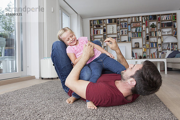 Mann liegt auf dem Boden und spielt mit seiner kleinen Tochter.