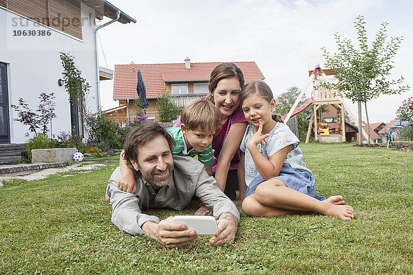 Lächelnde vierköpfige Familie im Garten mit Handy