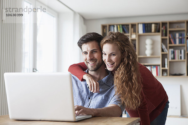Glückliches Paar zu Hause mit Blick auf den Laptop