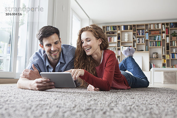 Glückliches Paar auf dem Boden liegend mit digitalem Tablett