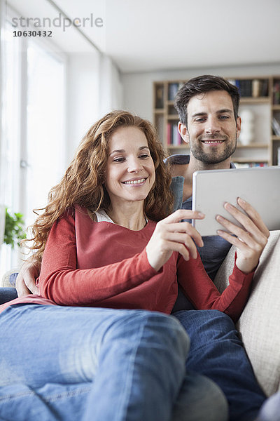 Entspanntes Paar zu Hause auf der Couch mit digitalem Tablett
