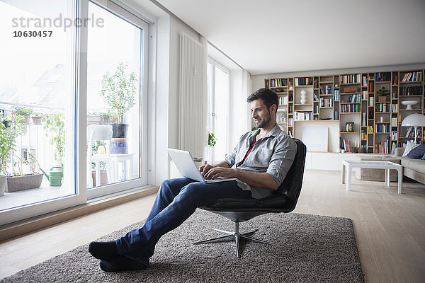 Mann zu Hause sitzend im Sessel mit Laptop