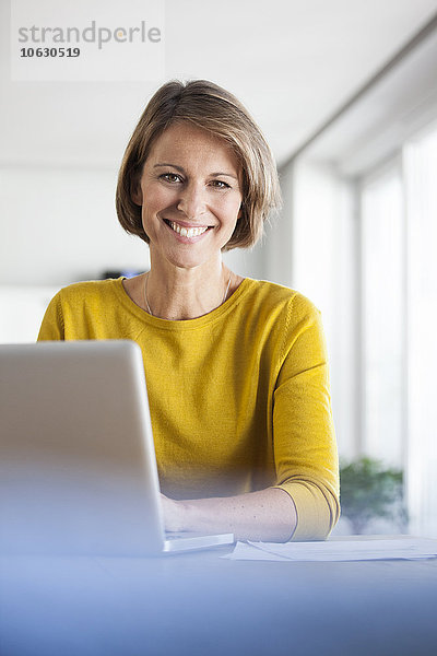 Porträt einer lächelnden Frau zu Hause mit Laptop