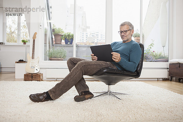 Erwachsener Mann zu Hause im Sessel sitzend mit digitalem Tablett