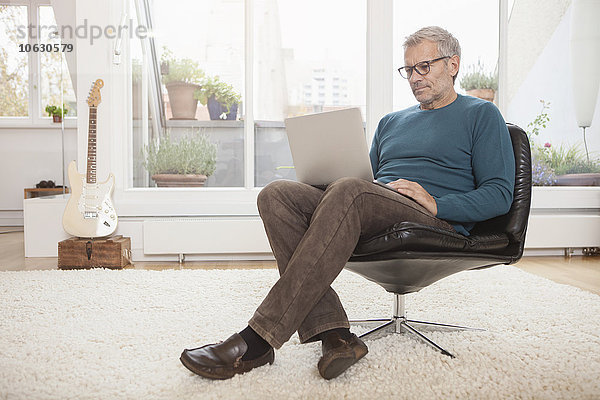 Erwachsener Mann zu Hause sitzend im Stuhl mit Laptop