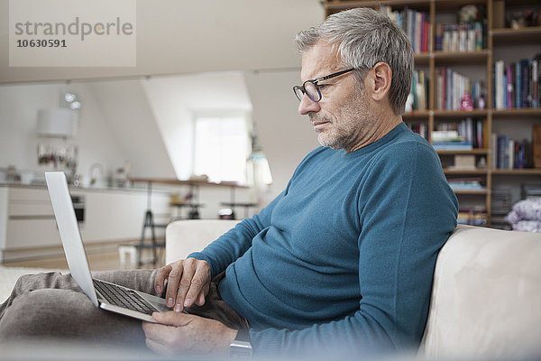 Erwachsener Mann zu Hause sitzend auf der Couch mit Laptop