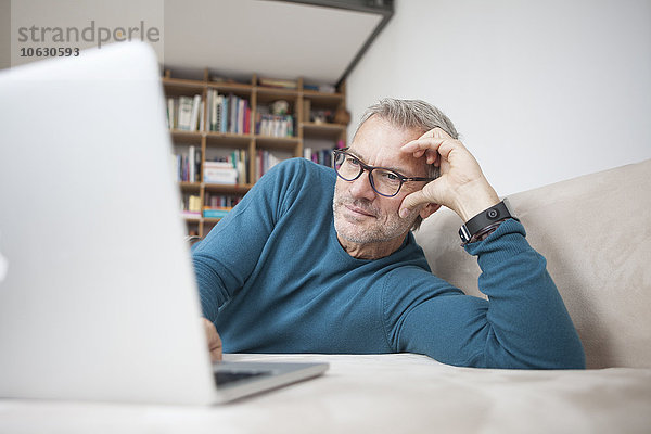 Erwachsener Mann zu Hause auf der Couch liegend mit Laptop