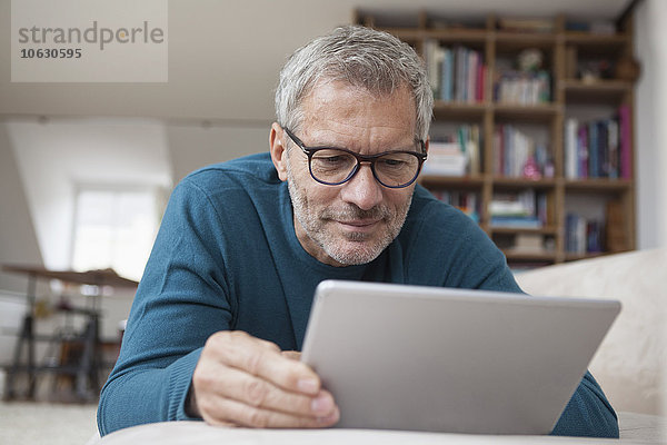 Erwachsener Mann zu Hause auf der Couch liegend mit digitalem Tablett