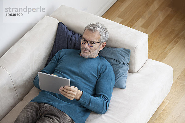 Erwachsener Mann zu Hause auf der Couch liegend mit digitalem Tablett