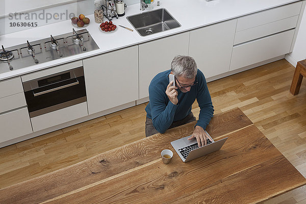 Erwachsener Mann in der Küche mit Handy und Laptop