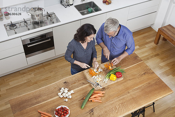 Reife Paare bereiten Gemüse in der Küche zu.