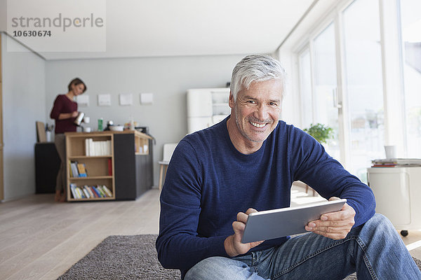 Porträt eines lächelnden Mannes zu Hause auf dem Boden sitzend mit digitalem Tablett