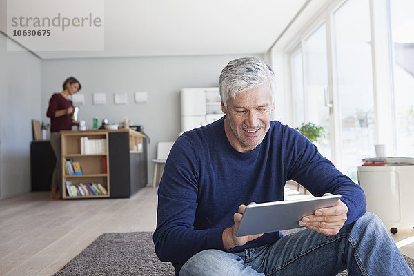 Mann sitzt zu Hause auf dem Boden und benutzt ein digitales Tablett.