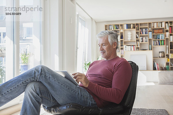 Der reife Mann entspannt sich zu Hause auf einem Ledersessel mit Hilfe eines digitalen Tabletts.