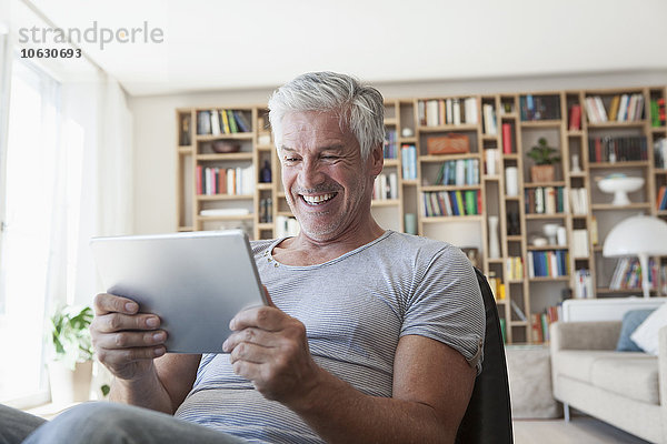 Porträt eines lachenden Mannes im Wohnzimmer mit Blick auf das digitale Tablett